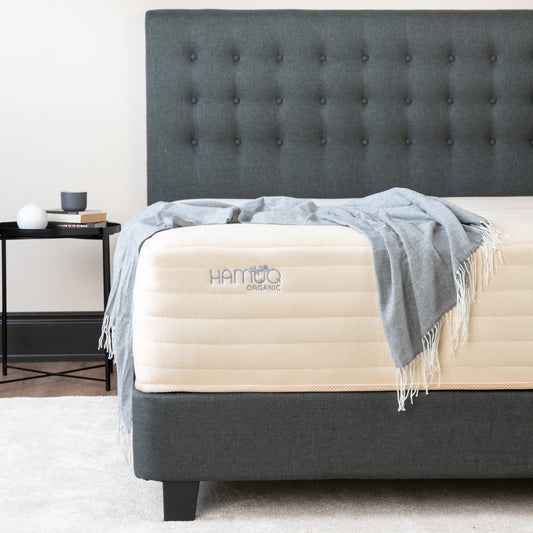 Hamuq Organic Hybrid mattress with a cream quilted cover and a grey throw blanket on a dark grey upholstered bed frame